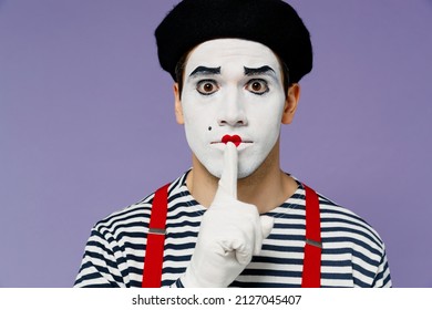 Close up secret vivid young mime man with white face mask wears striped shirt beret say hush be quiet with finger on lips shhh gesture isolated on plain pastel light violet background studio portrait
