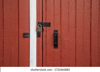 Close Up Of A Section Of A Red Barn Door With Black Hardware And A Padlock