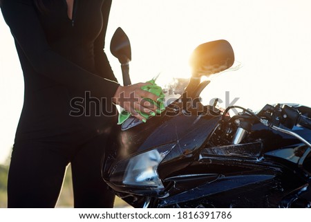 close up of seductive young woman's hand washing stylish sport motorcycle and wipes it from pink foam at sunrise.