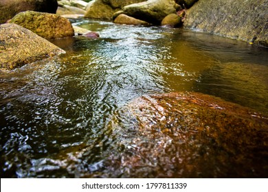 Close up and selected focus on water surface in small flowing stream in natural cascade at Hin Lad waterfall, Samui Island. Shining light reflection on surface of water flow between rock in nature.