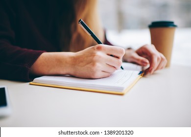 Close Up Of Selective Focus On Woman's Hands Writing Information To Textbook For Education Using Quality Black Pen, Cropped Image Of Female Sitting At Cafeteria Table With Notepad In Coffee Shop