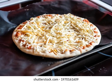 Close And Selective Focus Of A Readymade Frozen Stone Baked Thin Four Cheese Pizza On A Baking Mat Ready To Be Cooked In The Oven For Saturday Night Dinner