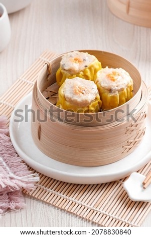 Close up and selective focus. Shumai is traditional Chinese dumpling also known as dim sum, snack that made from prawn, chicken and mushroom. Served on bamboo steamer, with spicy chilli sauce.