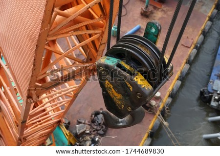 Close up and selective focused top view of hoist,hook,wire rope sling hanging on boom mobile crane placed on pontoon crane floating in river at construction site.Concept of industial.