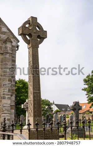 A close, selective-focus view of an ornate Celtic cross in a churchyard, showcasing its intricate stone carvings and craftsmanship against a softly blurred background.