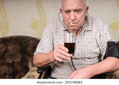 Close Up Senior Bald Man With BP Apparatus Attached On His Body, Taking His Medicine With A Glass Of Juice At The Living Room..