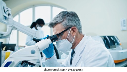 Close up of senior Caucasian male medical researcher work in lab on virus cure. Healthcare specialist man checking analysis through microscope, looking at blood cells, microbiology research concept