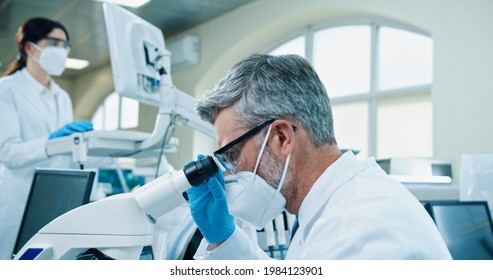 Close up of senior Caucasian male medical researcher work in lab on virus cure. Healthcare specialist man checking analysis through microscope, looking at blood cells, microbiology research concept
