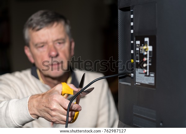 Stock photo of senior man cutting the cord of cable TV service