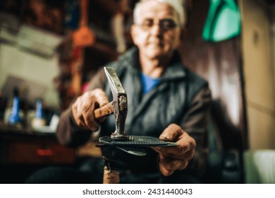 Close up of senior cobbler's hands hitting with hammer shoe sole while repairing footwear. Shoemaker hands repairing shoes at workshop. Small business owner is sitting at workshop and repairing shoe. - Powered by Shutterstock