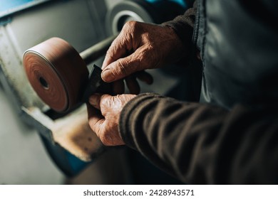 Close up of senior cobbler's hands using grindstone at his workshop for making footwear. Hands holding shoe part and fixing by using shoemaker tool. Senior man's hands using grindstone at workshop. - Powered by Shutterstock