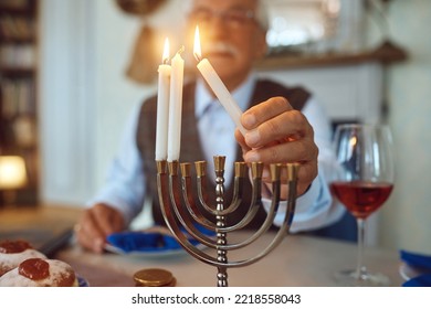 Cerca de un anciano celebrando Hanukkah mientras encienden velas en la menorah en casa. 