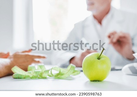 Close up of senior man doctor dietician meeting in medical office with patient at hospital. Focus on apple and measuring tape. Weightloss and burning calories. Eating disorder