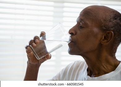 Close up of senior man drinking water against window in bathroom at home