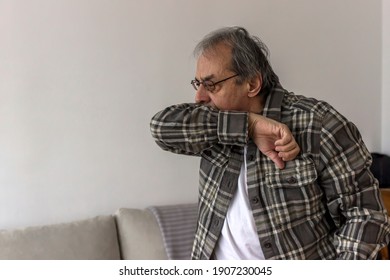 Close up of senior man with eyeglasses coughing into elbow at home. Frustrated elderly man sneezing and coughing into elbow in the living room. Health care and medical concept. Close up. - Powered by Shutterstock