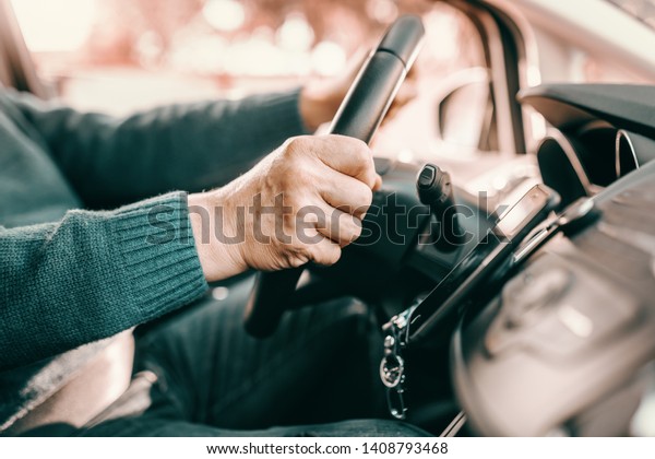 Close up of senior man holding hands on steering\
while and driving his\
car.