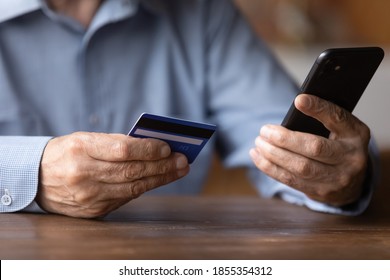 Close up senior man holding smartphone and plastic credit or debit card, mature customer paying online in store, entering information, browsing banking service, making secure internet payment