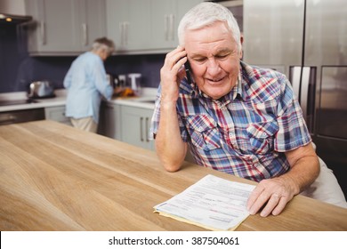 Close up of senior man talking on phone and woman working in kitchen at home