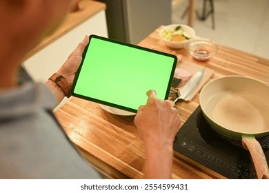 Close up of senior man using digital tablet in a cozy home kitchen to follow a recipe or cooking instructions - Powered by Shutterstock