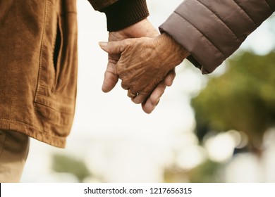 Close up of senior man and woman holding hands and walking outdoors. Rear view of old couple walking hand in hand outdoors.