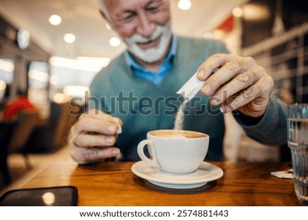 Close up of senior man's hands adding bag of sugar into coffee at coffee shop.