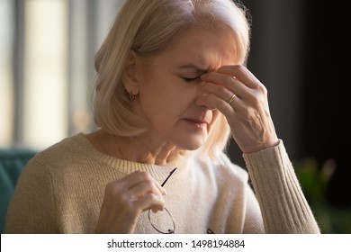 Close up of senior old lady feel unhealthy touch massage eyes having strong migraine symptoms or headache, elderly woman take off glasses suffering from dizziness, hypertension, sight problem concept