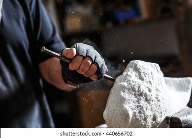 Close up of senior sculptor hands working on his marble sculpture in his workshop with hammer and chisel.