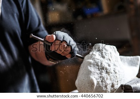 Close up of senior sculptor hands working on his marble sculpture in his workshop with hammer and chisel.