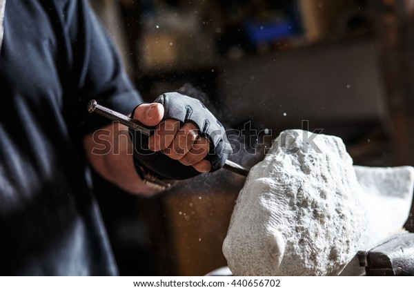 Close up of senior\
sculptor hands working on his marble sculpture in his workshop with\
hammer and chisel.