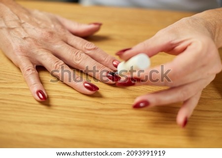 Close up Senior woman applying polish on nails at home, aged female painting fingernails with colorless protective enamel, Beauty treatment and hand care concept