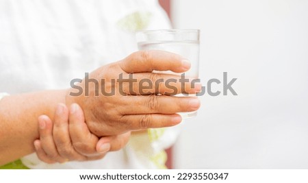 close up senior woman hand hold glass of waster for drink with unsteady at home for mature lifestyle and Parkinson's symptom concept