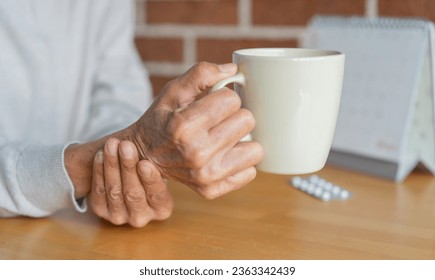 close up senior woman hold on hand to relief shaky symptom while drink water for Parkinson’s disease and chronic illness health care concept - Powered by Shutterstock