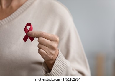 Close up of senior woman hold red ribbon breast cancer symbol support people patient with illness, middle-aged female volunteer keep AIDS HIV disease awareness, elderly healthcare, medicine concept