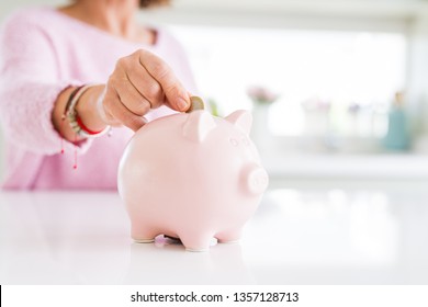 Close up of senior woman putting a coin inside piggy bank as savings Stock Photo
