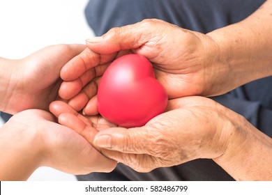 Close Up Of Senior Woman And Young Female Hands Holding Red Heart.National Family Caregivers Month, National Hospice Month And National Home Care Month. Age, Family, Love And Health Care Concept 