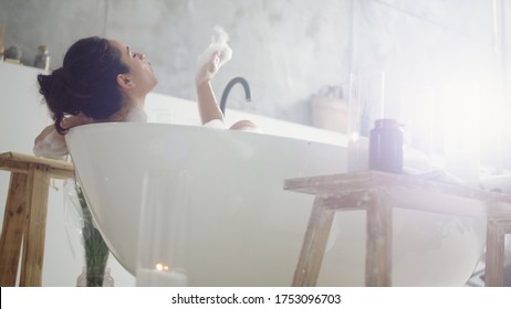 Close up sensual woman blowing foam in slow motion. Bottom view of sexy girl playing with bubbles in bathtub at home. Smiling girl having fun with foam in luxury bath.