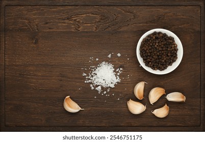 Close up separated garlic cloves, black peppercorns and coarse sea salt on a dark brown rustic wooden cutting board, top down view, directly above - Powered by Shutterstock