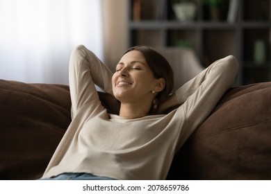 Close Up Of Serene Peaceful Smiling 30s Woman Lean On Sofa With Hands Behind Head Closing Eyes Breath Fresh Conditioned Air Inside Modern Cozy Living Room. Carefree No Stress Day Off, Leisure Concept