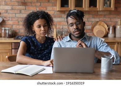 Close Up Serious African American Couple Looking At Laptop Screen, Sitting At Table In Kitchen, Focused Wife And Husband Browsing Online Banking Service, Checking Taxes, Bills, Searching Information