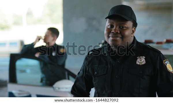 Close up serious face young african american man\
cops stand near patrol car look at camera enforcement officer\
police uniform auto safety security communication control policeman\
close up slow motion