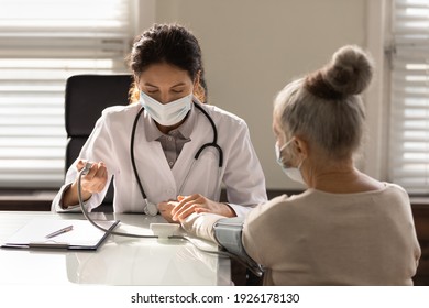 Close Up Serious Female Doctor Wearing Face Mask Measuring Checking Old Woman Blood Pressure, Using Digital Tonometer, Medical Checkup, Elderly Generation Healthcare And Insurance Concept