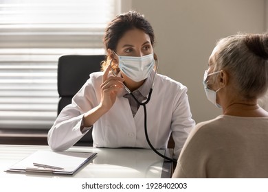 Close Up Serious Female Doctor Wearing Face Mask And Coat Checking Senior Patient Lungs, Listening To Heartbeat, Mature Woman Breath, Elderly Generation Healthcare, Medical Checkup Concept