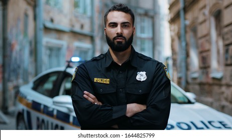 Close up serious young man cops hold pistol stand near patrol car look at camera enforcement officer police uniform auto safety security communication control policeman portrait slow motion