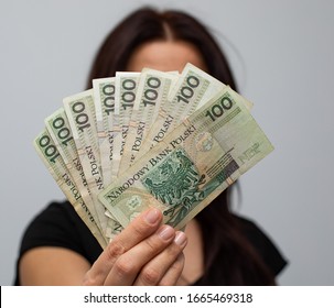 close up of several banknotes with a face value of PLN 100 Polish money, zloty held in a fan shape in the hands of a women on a grey background