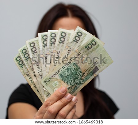 close up of several banknotes with a face value of PLN 100 Polish money, zloty held in a fan shape in the hands of a women on a grey background