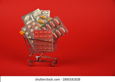 Close Up Several Different Blister Packs Of Pills In Small Shopping Cart Over Red Background, Concept Of Online Medicine Order Delivery, Low Angle View