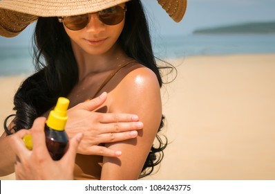 Close - Up Of Sexy Asian Woman Are Spray Sunscreen , Lotion Or Sunblock To Body For Prevent UV Rays From Sunlight Before The Sun Bathing In The Summer Or Vacation With Sea And Bluesky Bckground