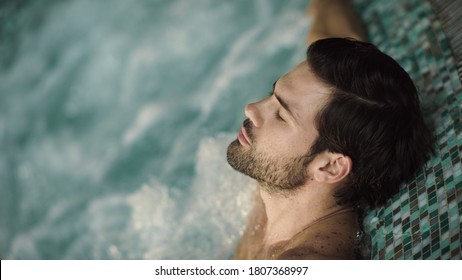 Close Up Of Sexy Man Enjoying Jacuzzi Spa In Slow Motion. Portrait Of Handsome Guy Relaxing In Pool At Wellness Hotel. Attractive Man Having Hydro Massage In Jacuzzi Indoor.