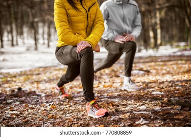 Close up of shape fitness girl in sportswear doing leg stretching with her personal trainer in the forest in the sunny winter morning.