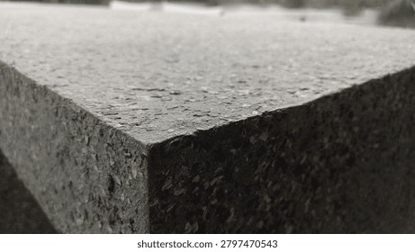 Close up of a sharp corner of a dark grey concrete bench with blurred background. Minimalist architectural texture for design backdrop, outdoor element, or copy space